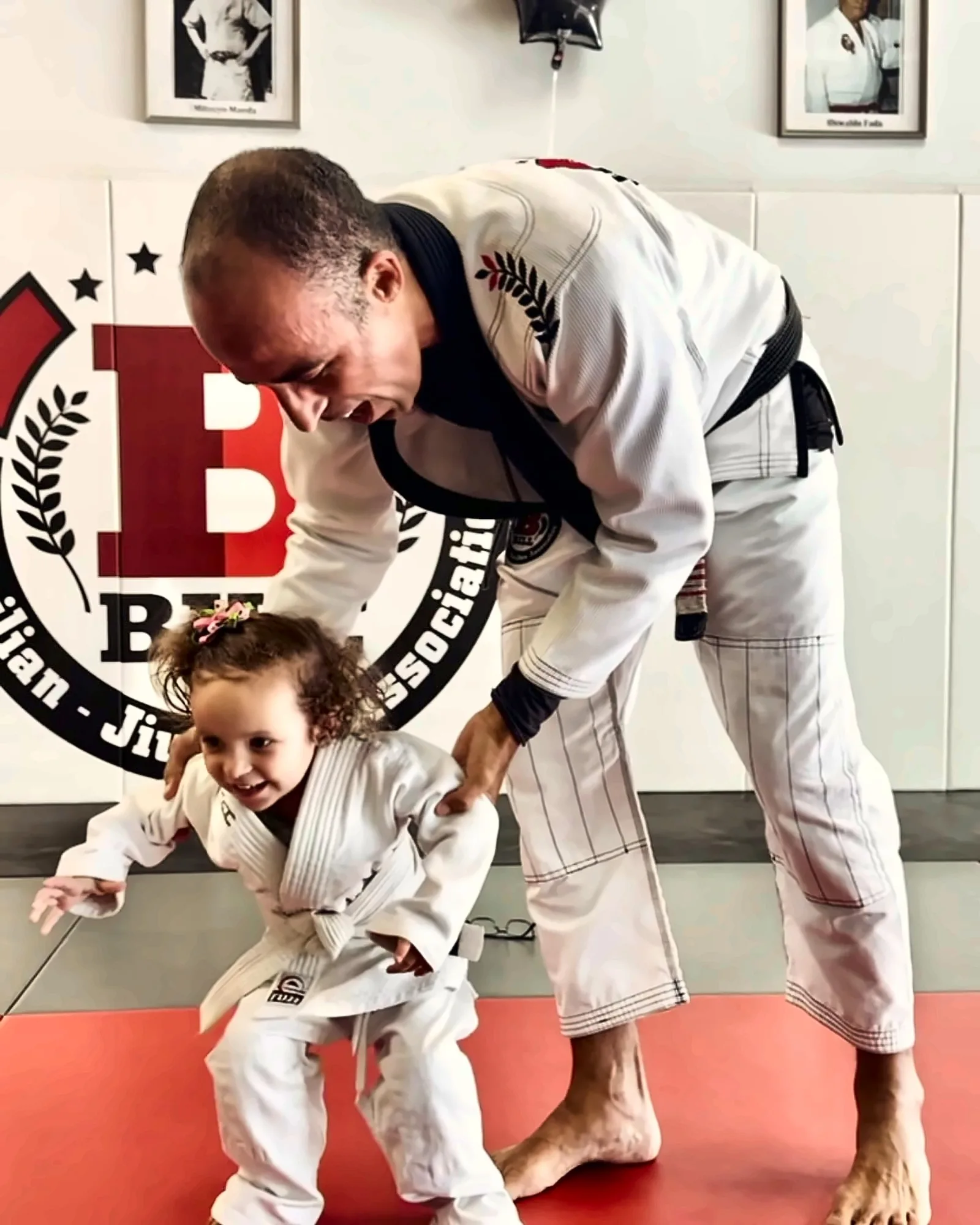 Professor Bill bending down to guide a very young student in a white gi